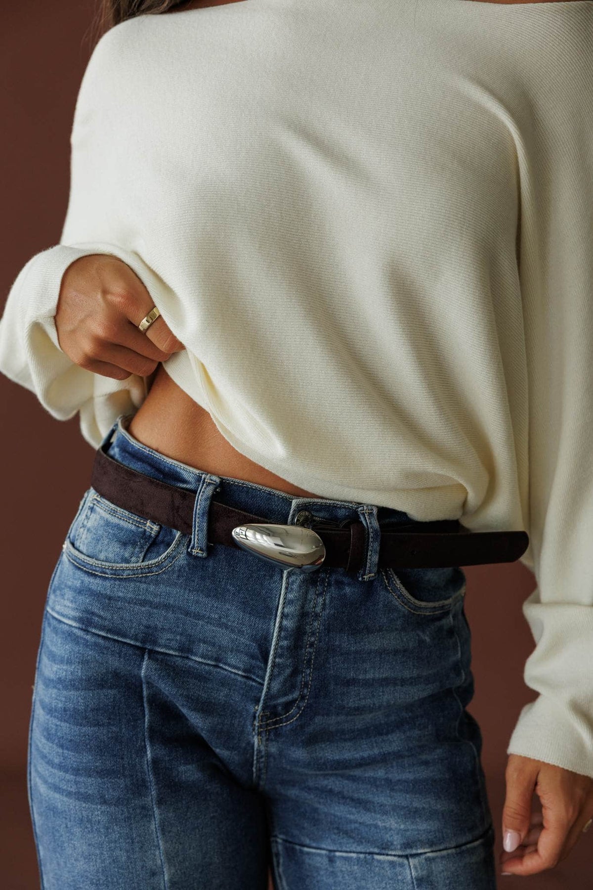 Boston Belt, in dark chocolate suede, close front view of the oval buckle over denim