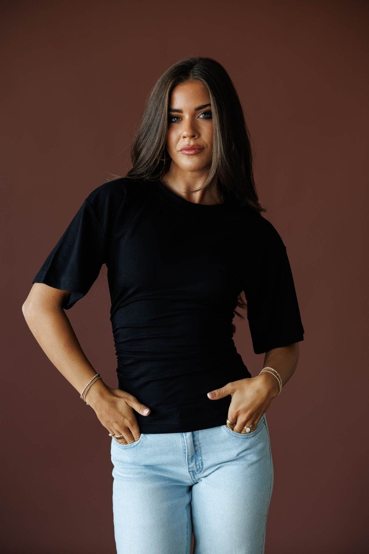 One Sided Ruched Tee in black, front view on model with light wash jeans, hands on hips