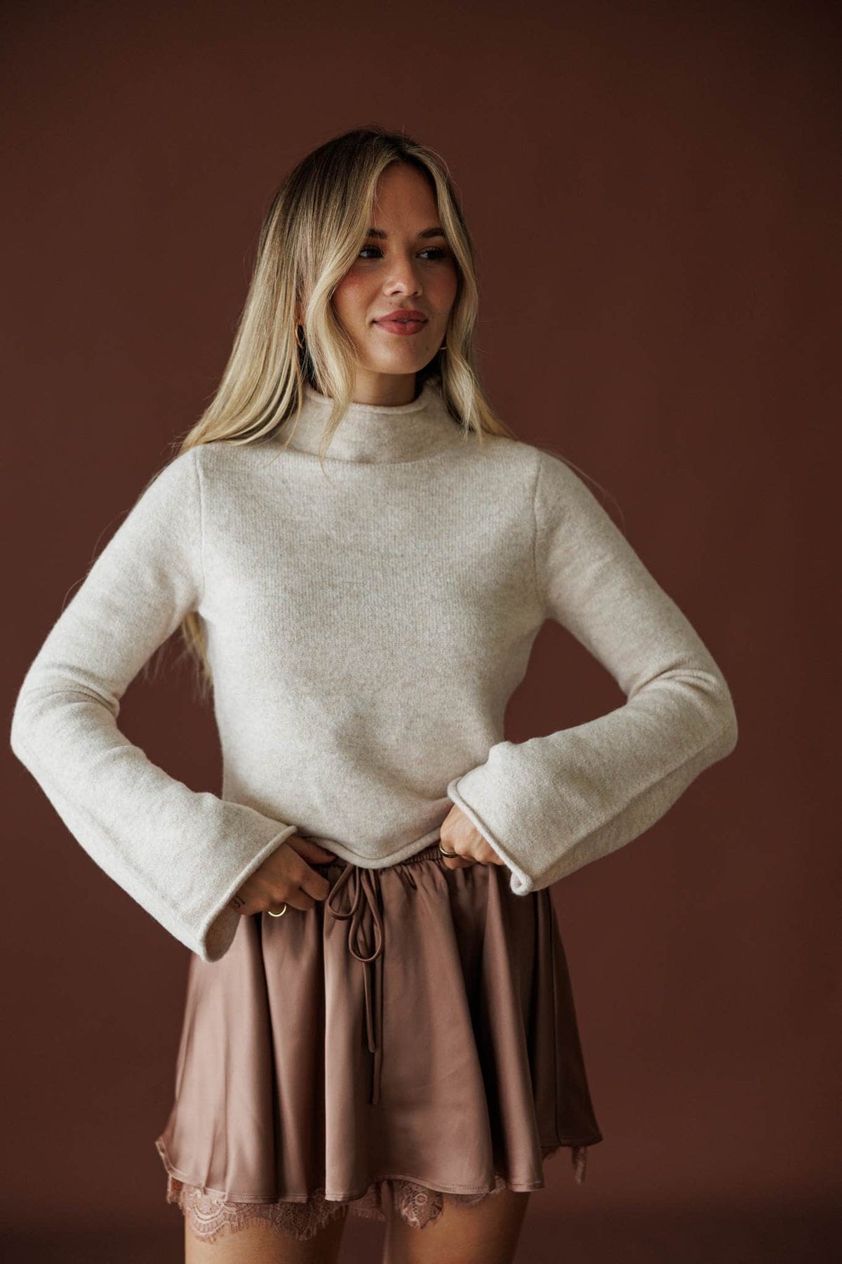 The Cozy Classic Sweater in oatmeal, front view of the mock neck worn with a satin skort