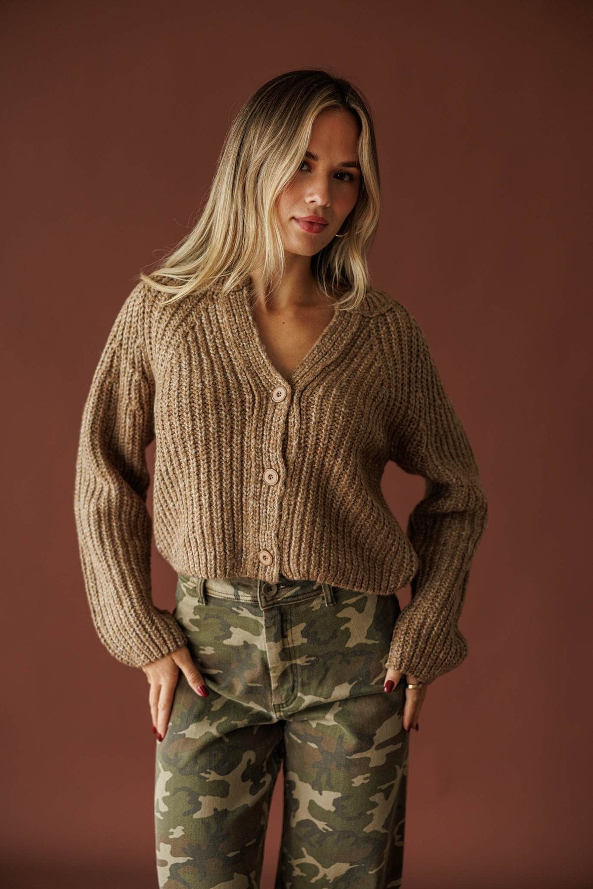 Cedar House Cardigan in sand, front view of the chunky V-neck knit worn open over camo pants