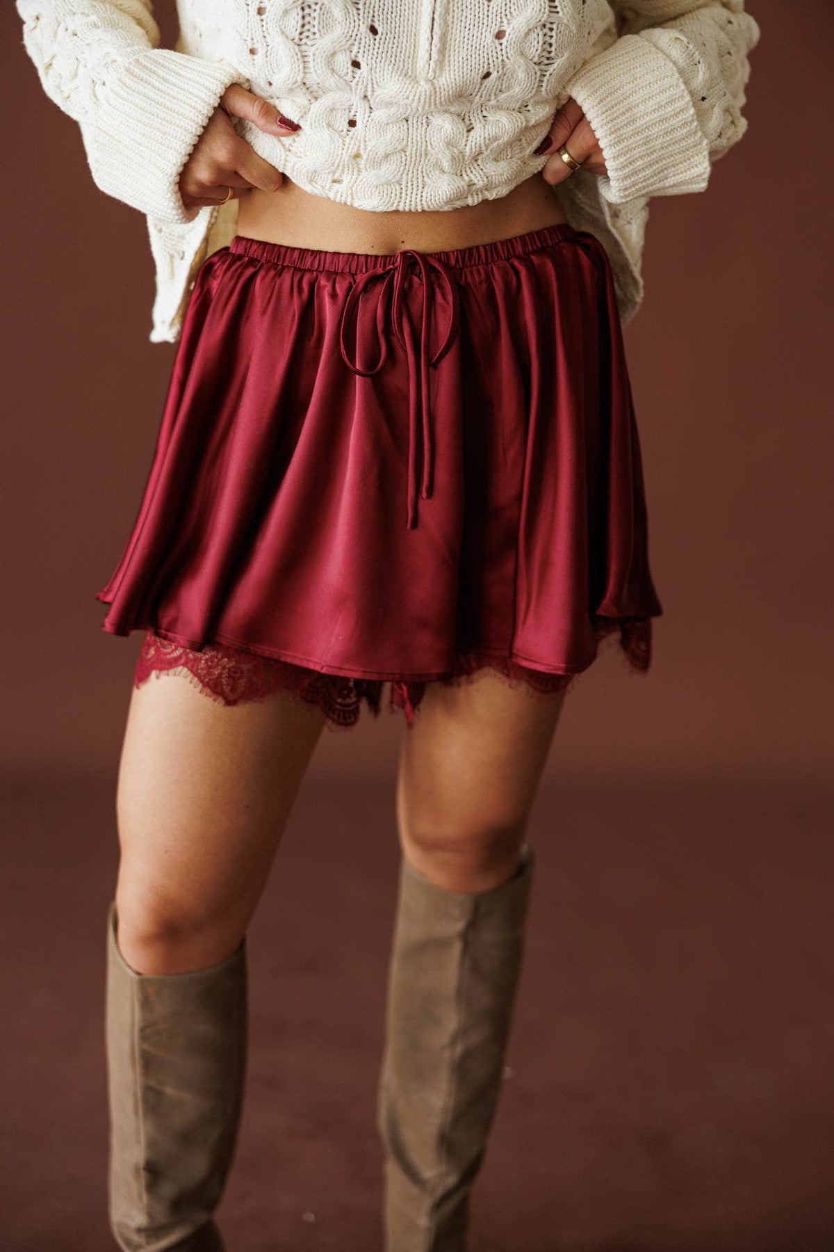 Satin And Lace Skort in burgundy, front view of the lace-trimmed hem with tall boots