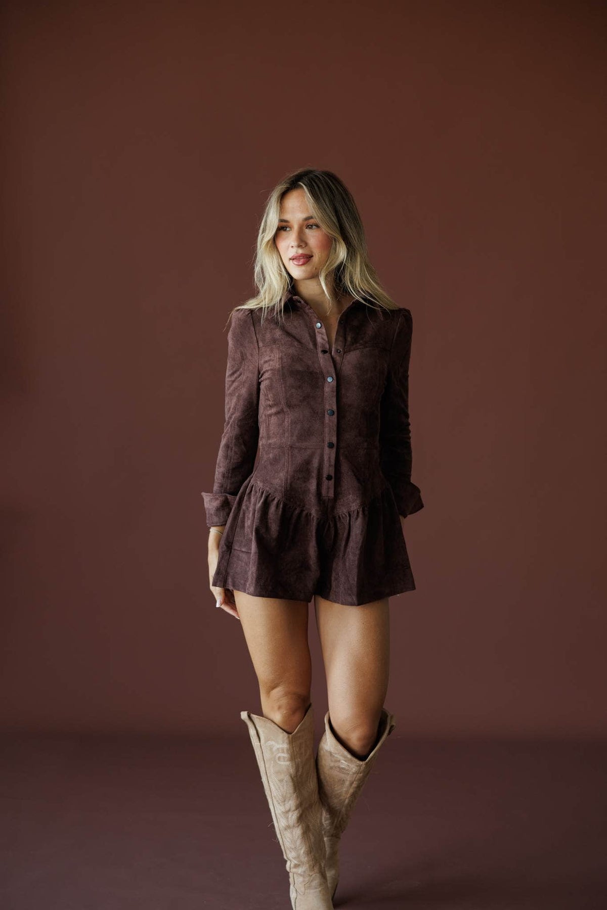 The Outrider Romper in chocolate, full-length view on model with tall cream boots