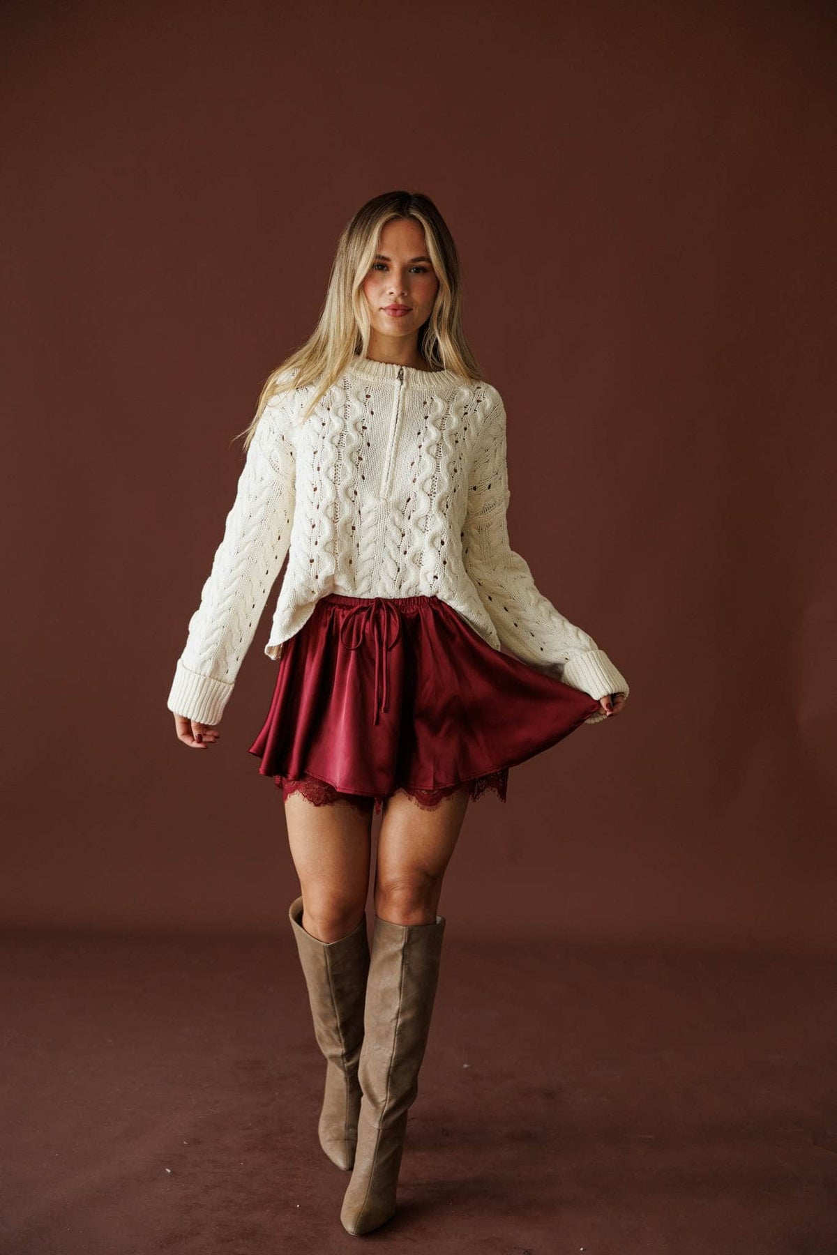 Cable Me Later Sweater in cream, full-length walking view over a burgundy satin skirt